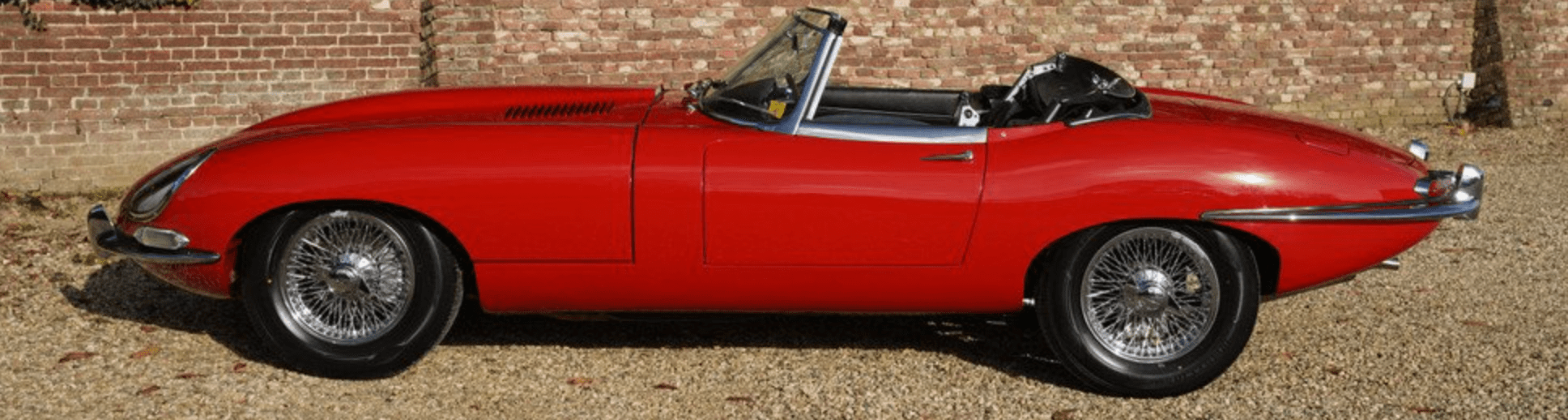 Red vintage convertible car parked on gravel.