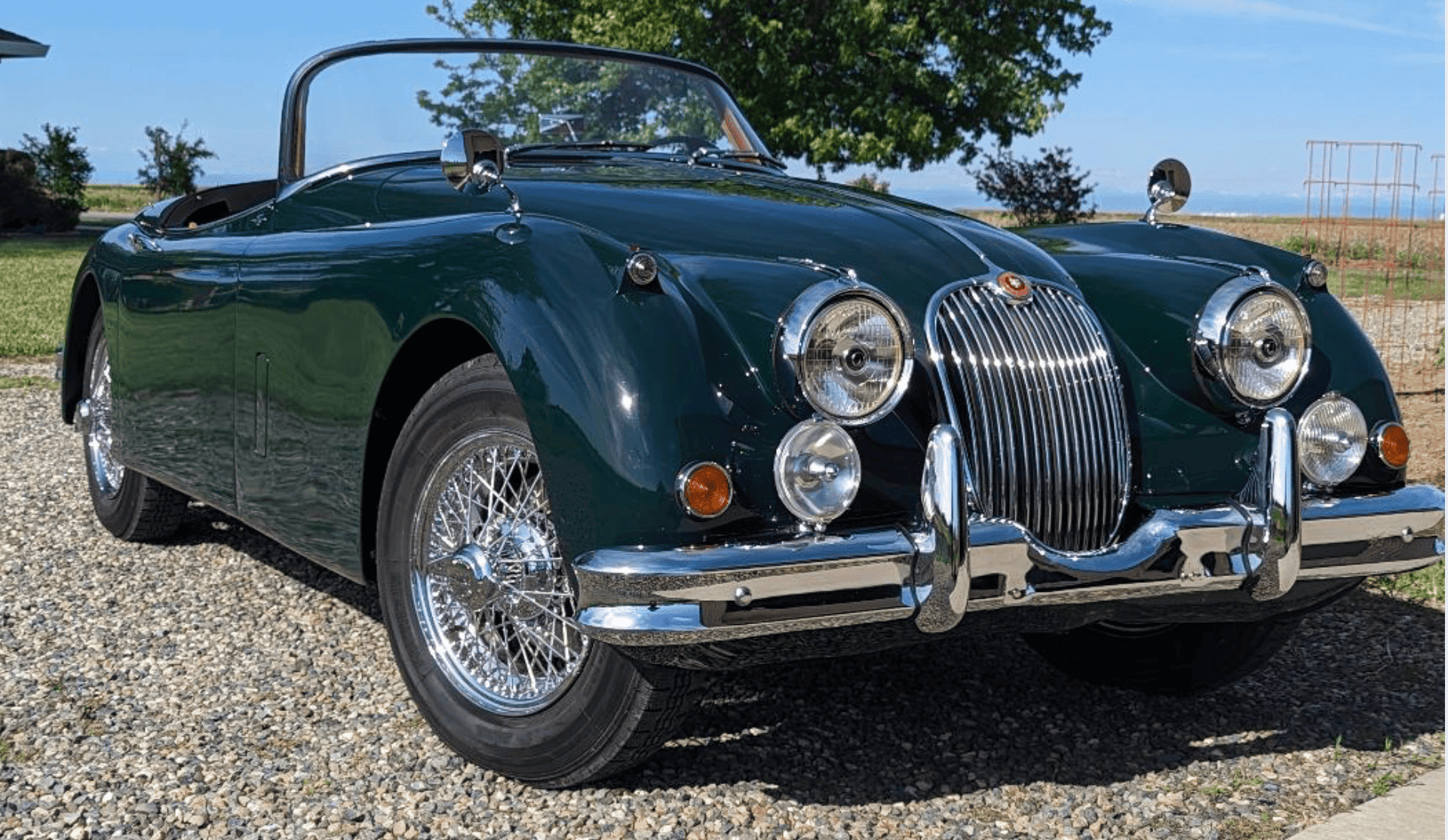 Classic green convertible car on gravel driveway.